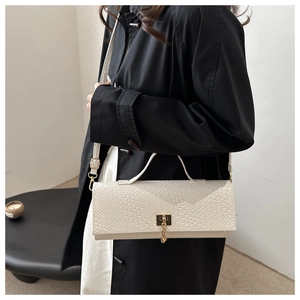 Detalle de bolso rectangular crema con textura de cocodrilo y cierre metálico dorado
