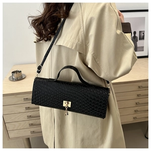 Detail of woven texture and gold clasp on a black crossbody baguette bag worn with trench coat