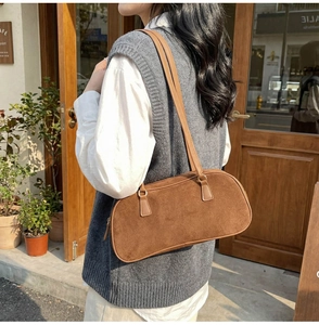 Brown suede baguette bag worn on the shoulder by a model in a street setting