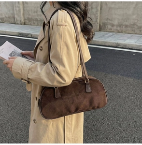 Detail of dark brown suede shoulder bag worn with a classic trench coat outdoors
