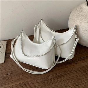 White faux leather tote bag with silver chain detail on a dark wooden surface