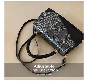 Detail of adjustable shoulder strap and gold hardware on snake-print square bag