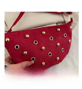 Détail du sac demi-lune en daim rouge avec rivets dorés et œillets métalliques