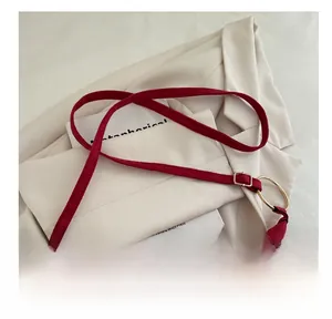 Gros plan sur un sac bandoulière en daim rouge foncé avec rivets et œillets dorés