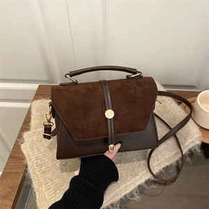 Petit sac bandoulière en daim marron foncé avec détails dorés sur une table