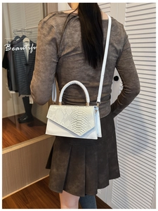Detail of white leather handbag featuring textured python pattern and gold hardware accents