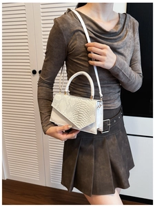 Close-up of white leather handbag featuring snake-embossed texture and gold buckles
