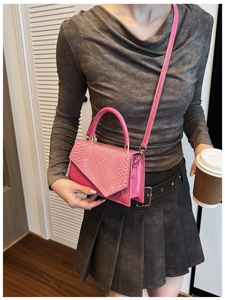 Detail of pink faux crocodile leather handbag held by model in casual street style
