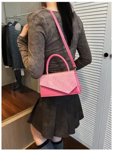 Detail of pink snake-embossed leather handbag shown on a model for crossbody styling