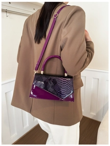 Detail view of purple snakeskin textured square bag worn by a model in a brown suit