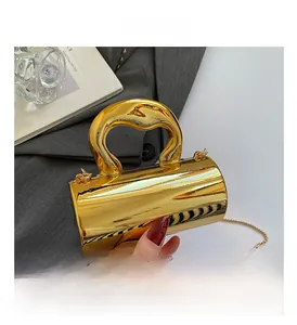 Detail of glossy gold cylindrical handbag with artistic handle and metallic chain strap