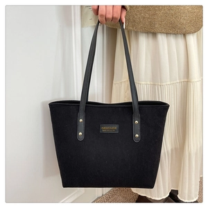 Detail of black corduroy tote bag featuring a leather patch and slim leather shoulder straps