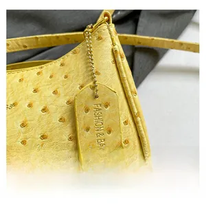 Dettaglio macro della trama a struzzo gialla e targhetta sulla borsa a spalla da donna