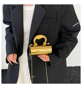 Macro detail of golden cylindrical mini bag with unique wavy handle and slim chain strap