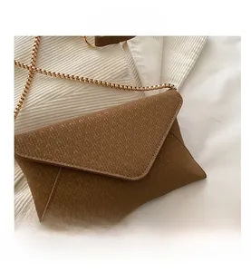 Close-up of brown envelope shoulder bag featuring woven texture and gold chain link strap