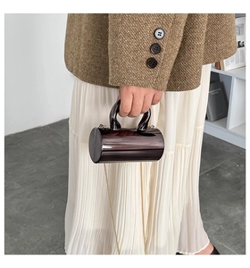 Detail of gunmetal cylindrical bag with high-gloss mirror finish and metal chain strap