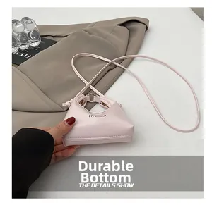 Dettaglio di una mini borsa a tracolla rosa con logo minimalista su sfondo bianco curato