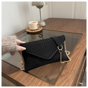 Detail of black envelope clutch with V-shaped woven texture and gold chain strap