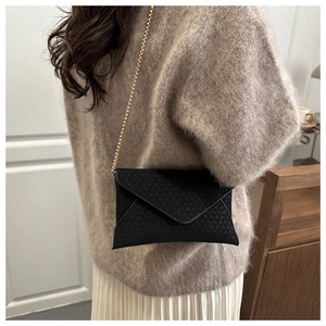 Detail of black woven envelope bag featuring elegant gold chain strap for women