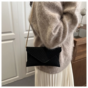 Close-up of elegant black envelope crossbody bag with gold chain strap on model