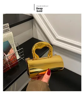 Detail of deep gold acrylic cylindrical handbag with wavy handle and metal chain strap