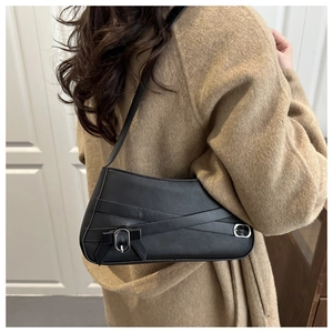 Dettaglio della borsa a spalla nera con fiocco indossata su un cappotto marrone