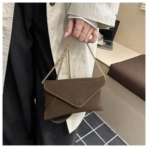 Close-up of brown textured leather envelope bag with gold chain strap on a trench coat