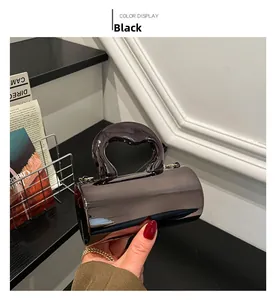 Detail of a shiny black cylindrical handbag featuring a thick curved top handle and metal hooks