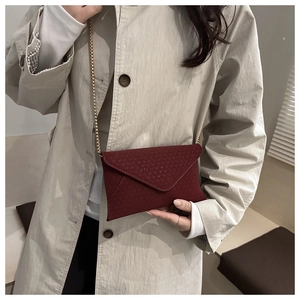 Detail of burgundy envelope clutch bag with V-quilted texture and gold chain strap