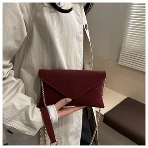 Detail of burgundy envelope crossbody bag with textured pattern and gold chain strap