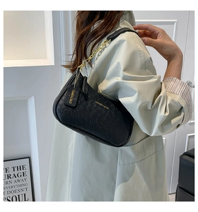 Dettaglio della borsa a spalla nera testurizzata con catena dorata su un trench coat