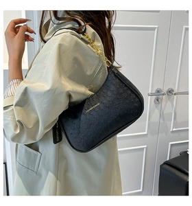 Dettaglio della borsa hobo nera testurizzata struzzo con catena dorata su un trench beige