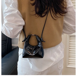 Dettaglio di una mini borsa in pelle verniciata nera con logo e tracolla sottile