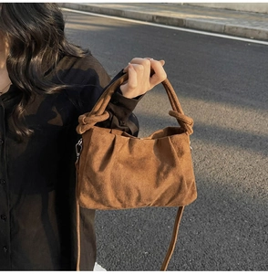 Détail d'un sac en daim marron avec design plissé et poignée à nœud en décor urbain