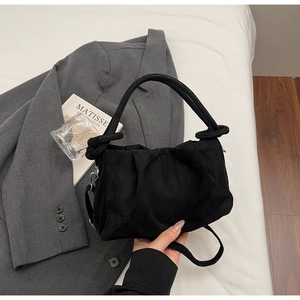 Détail du sac à main plissé noir en texture suédine sur un blazer gris et un livre
