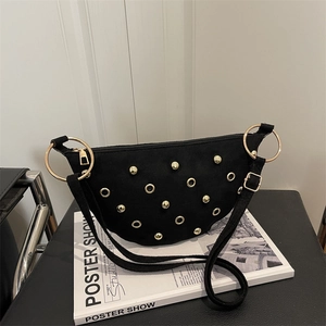 Chic black crescent shoulder bag with gold studs and large rings on a fashion book
