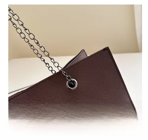 Dettaglio borsa in pelle litchi marrone scuro con occhiello in metallo e tracolla a catena