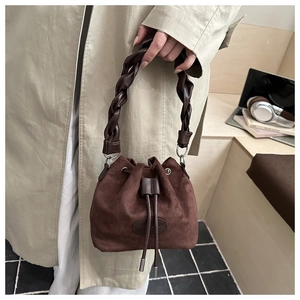Detail of dark brown suede bucket bag featuring woven handle and drawstring closure