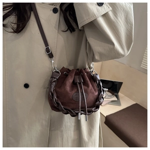 Detailed view of the dark brown suede bucket bag featuring chunky leather braided trim
