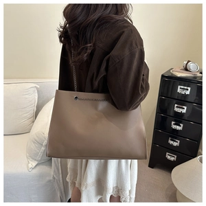 Dettaglio borsa tote in pelle marrone con catena d'argento indossata da una modella