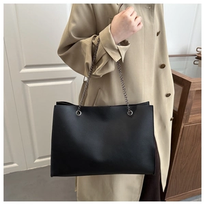Dettaglio borsa tote in pelle nera con tracolla a catena su un trench