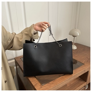 Dettaglio borsa tote nera in pelle martellata con catena d'argento indossata con un trench