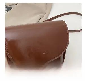 Detail shot of brown saddle bag showing the HYLLZZA logo and smooth leather texture