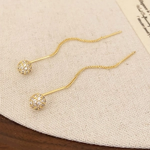 Detail of long gold dangling earrings with shimmering pave zircon spheres on linen texture