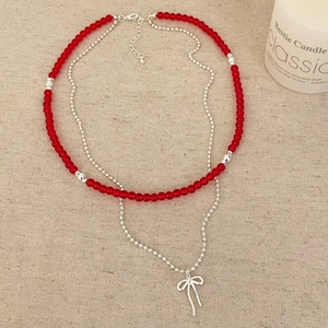 Collier double rang avec perles rouges et pendentif nœud argenté sur fond en lin