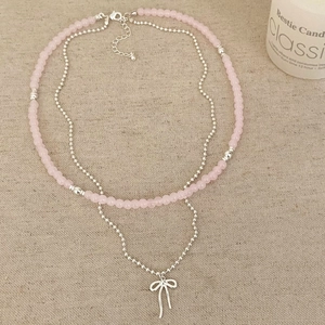 Détail d'un collier double rang perles roses et pendentif nœud argenté sur lin