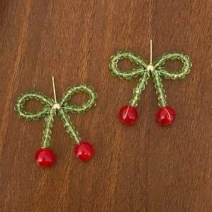 Detail view of handmade beaded cherry earrings with green crystals on wood background