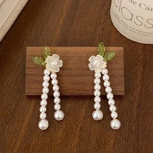 Elegant gold-plated flower earrings with white pearl tassels on a wooden display