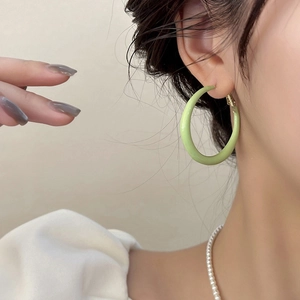 Gros plan de créoles vert clair en émail mat portées par un mannequin pour la taille