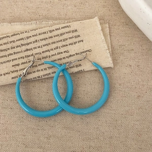 Close-up of bright blue resin hoop earrings with smooth finish on vintage linen background